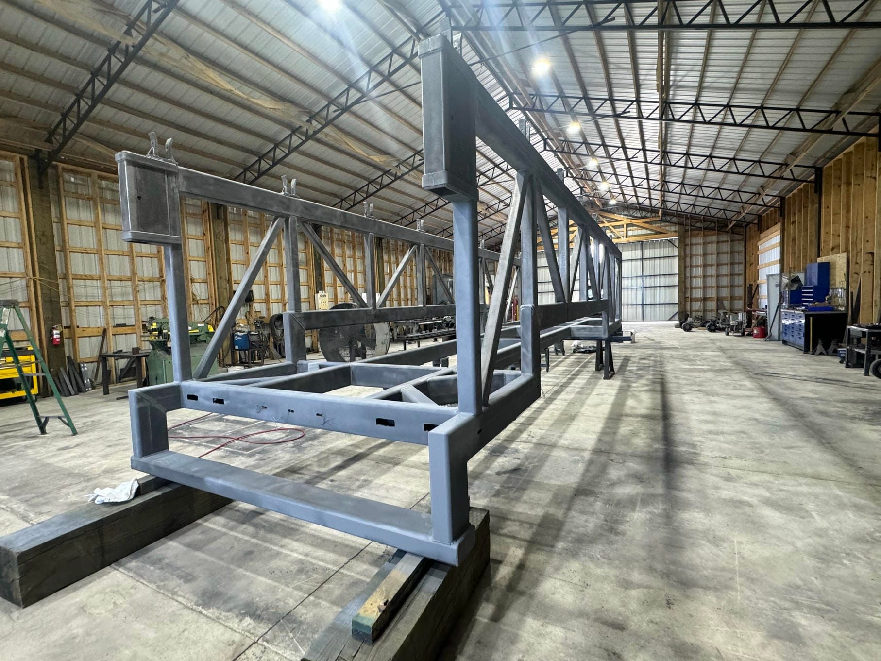 Large steel frame structure in a warehouse workshop, set on support beams with tools and equipment nearby