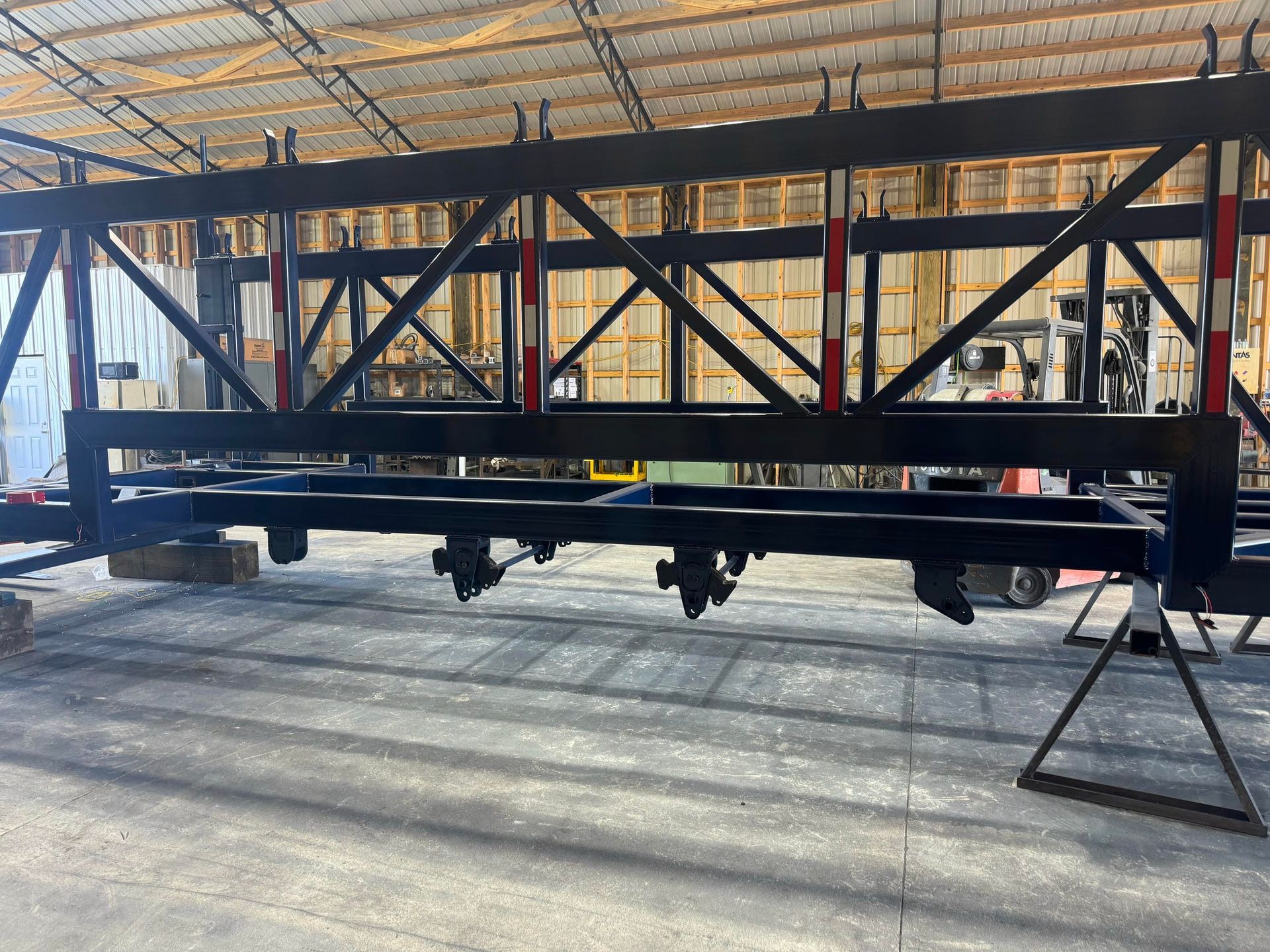 Black metal truss frame in a warehouse, supported on stands under a large canopy.