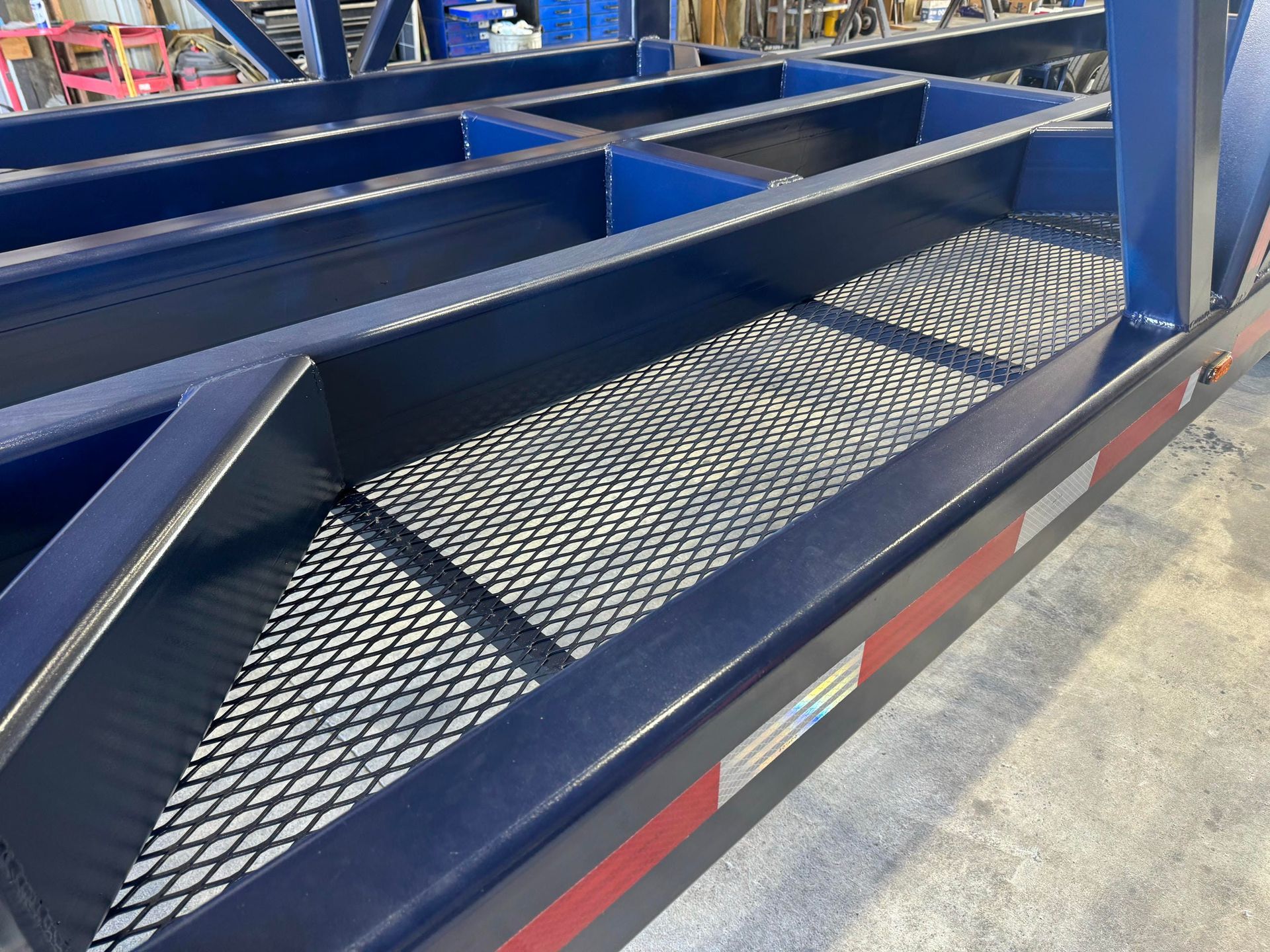 Blue metal trailer frame with diamond-plate ramps in a workshop