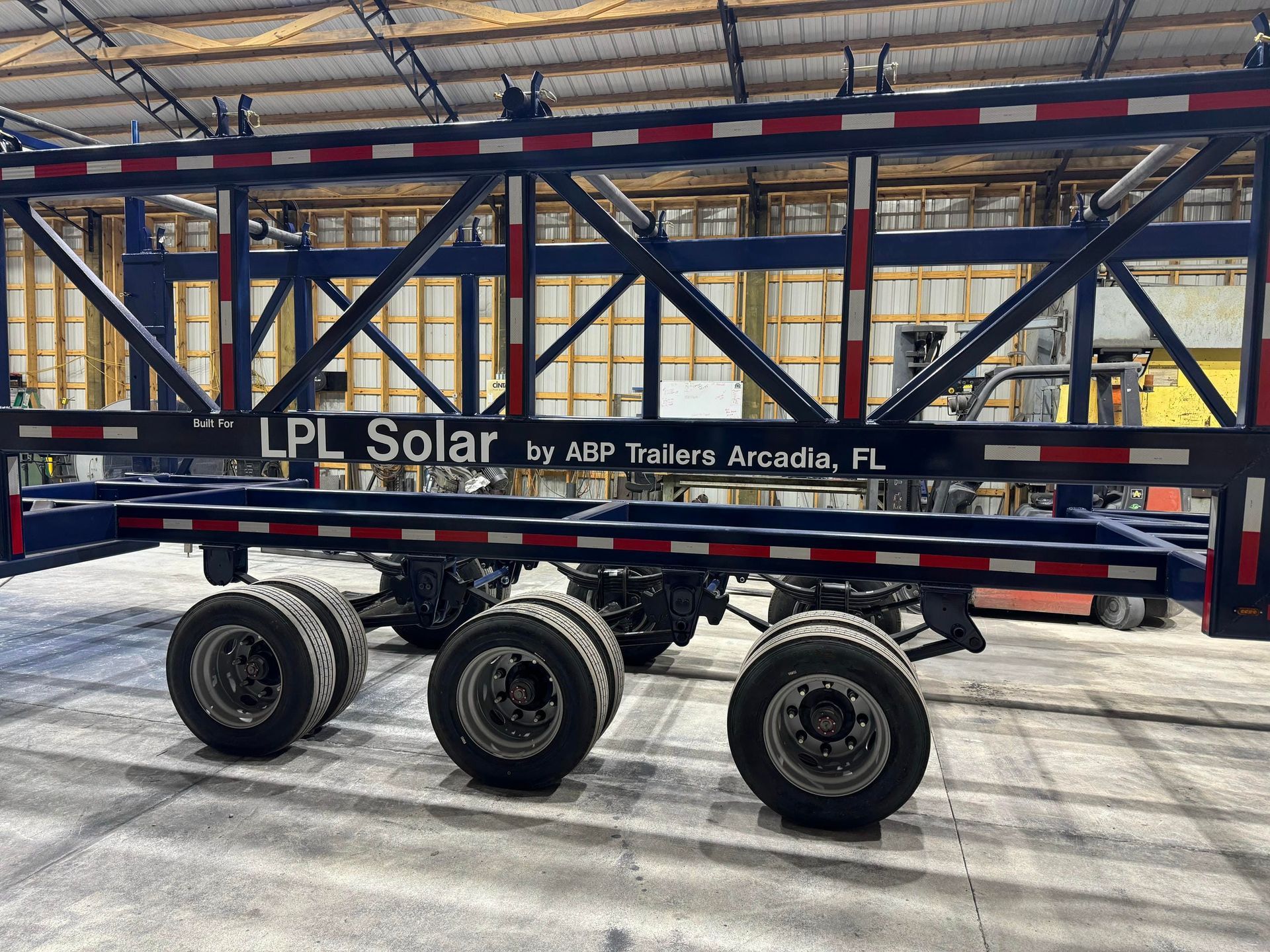 Black trailer with six wheels and metal frame inside a warehouse, labeled “LPC Solar” and “JDP Trucks Arcadia, FL.”
