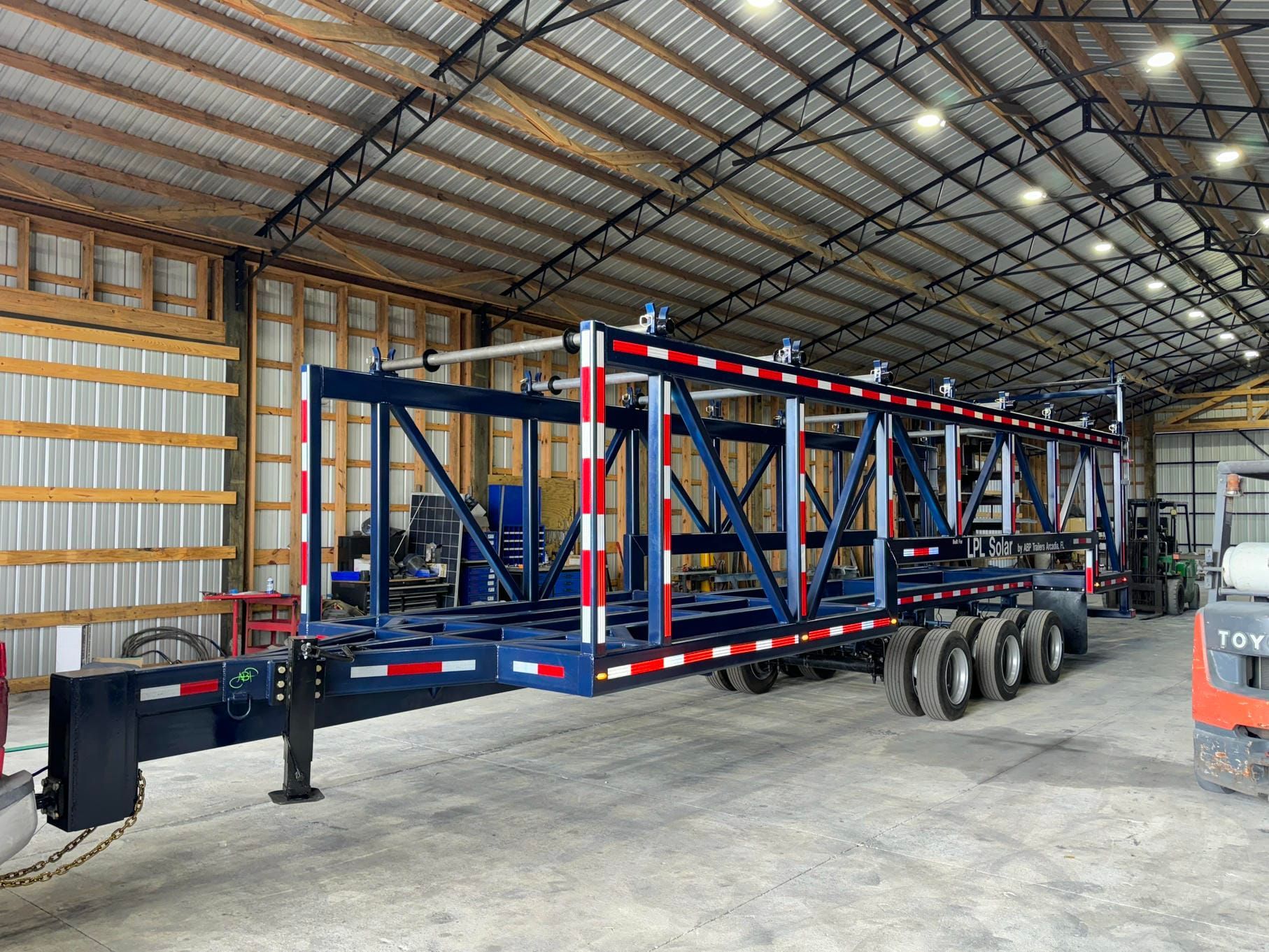 Large blue and red trailer frame inside a warehouse, with three axles and a forklift nearby