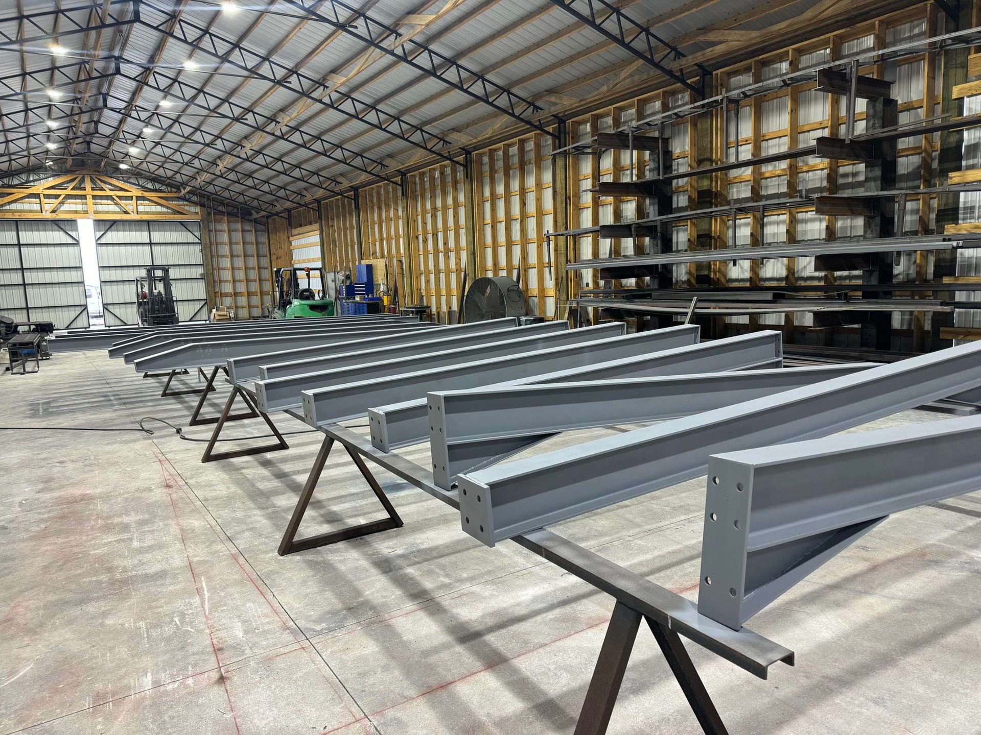 Steel beams on stands inside a large workshop or warehouse with shelving and construction materials.