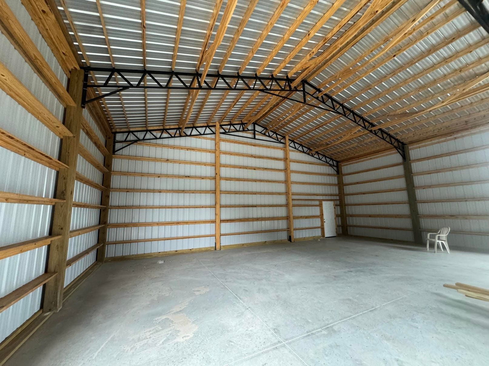 Empty metal-framed warehouse interior with corrugated walls, concrete floor, and a white chair in the corner