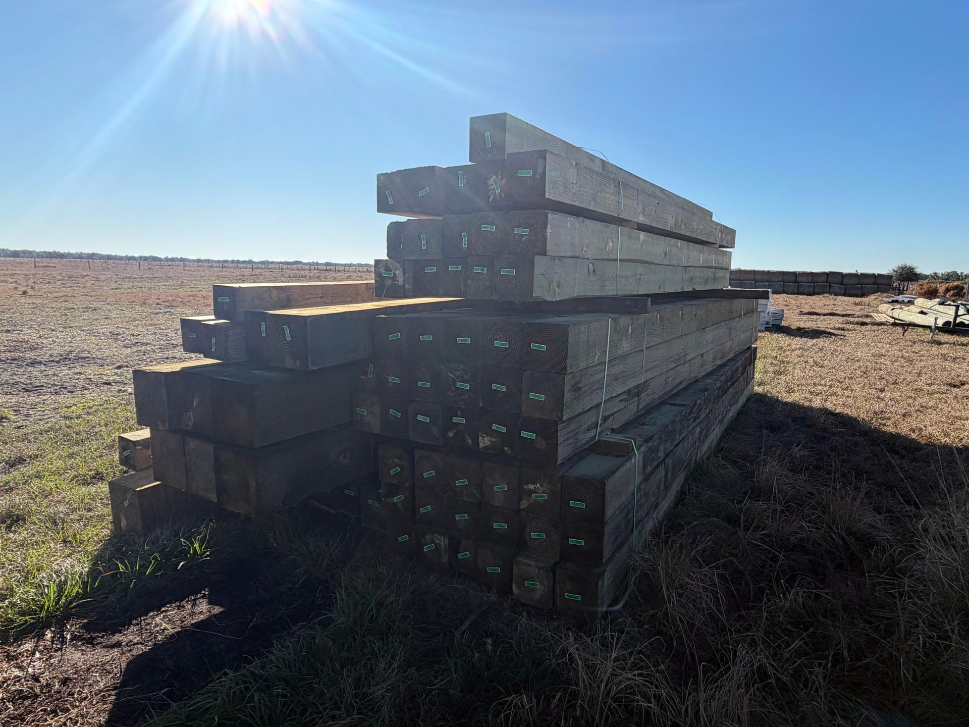 Stacked weathered wooden beams in a dry field under bright sunlight.