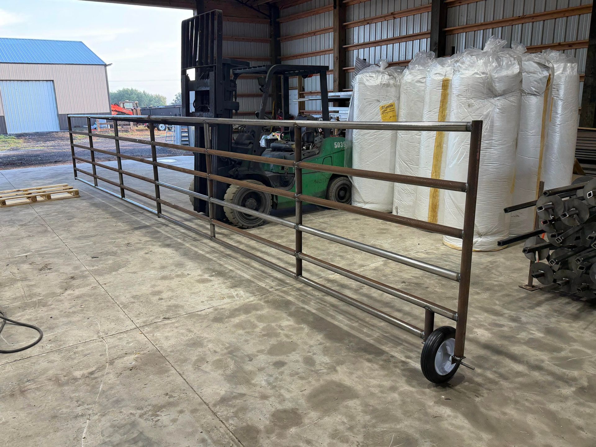 Metal gate panel on wheels in a warehouse, with a forklift and stacked white bags behind it.