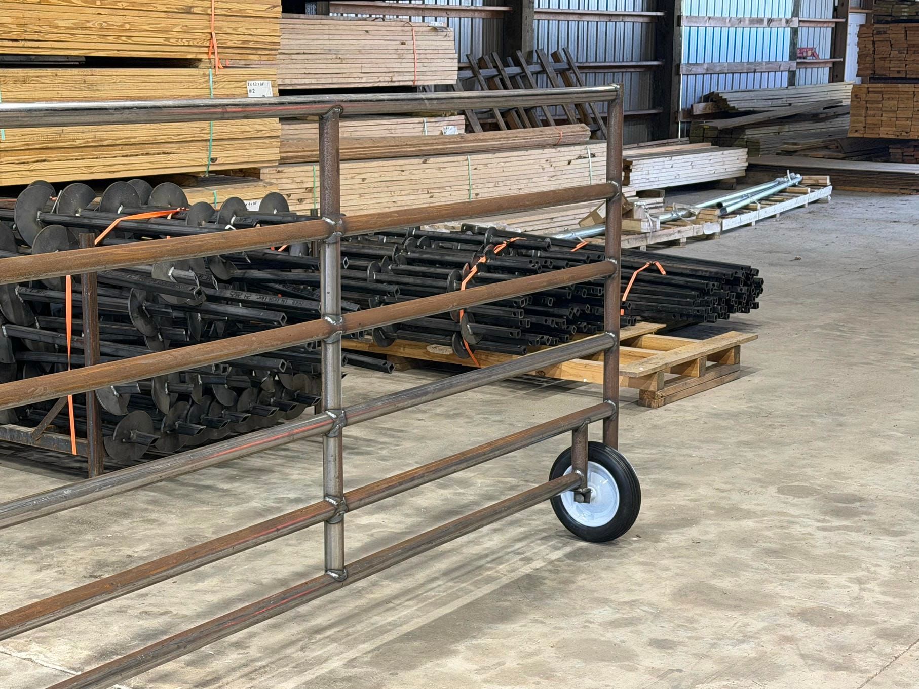 Metal cart with shelves and a single blue wheel in a warehouse beside stacked lumber and materials