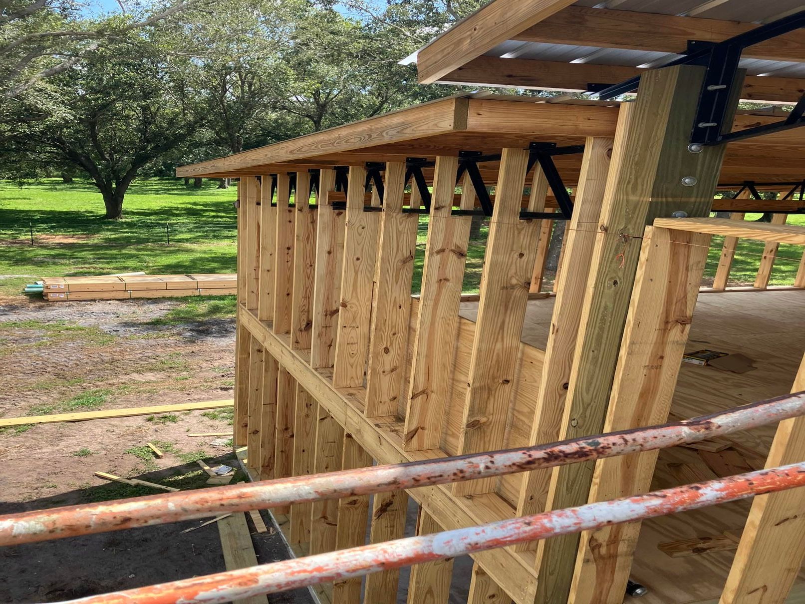 Wooden structure under construction with exposed framing and a slanted roof in a grassy outdoor area