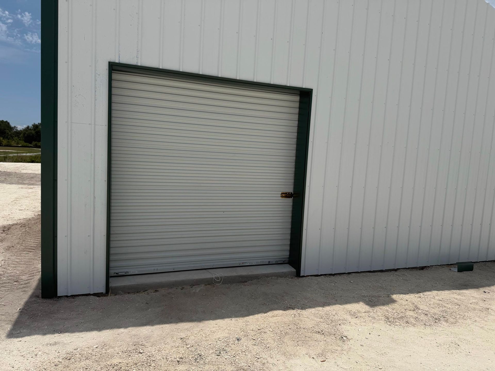 White roll-up door set in a gray metal building wall on a gravel lot.