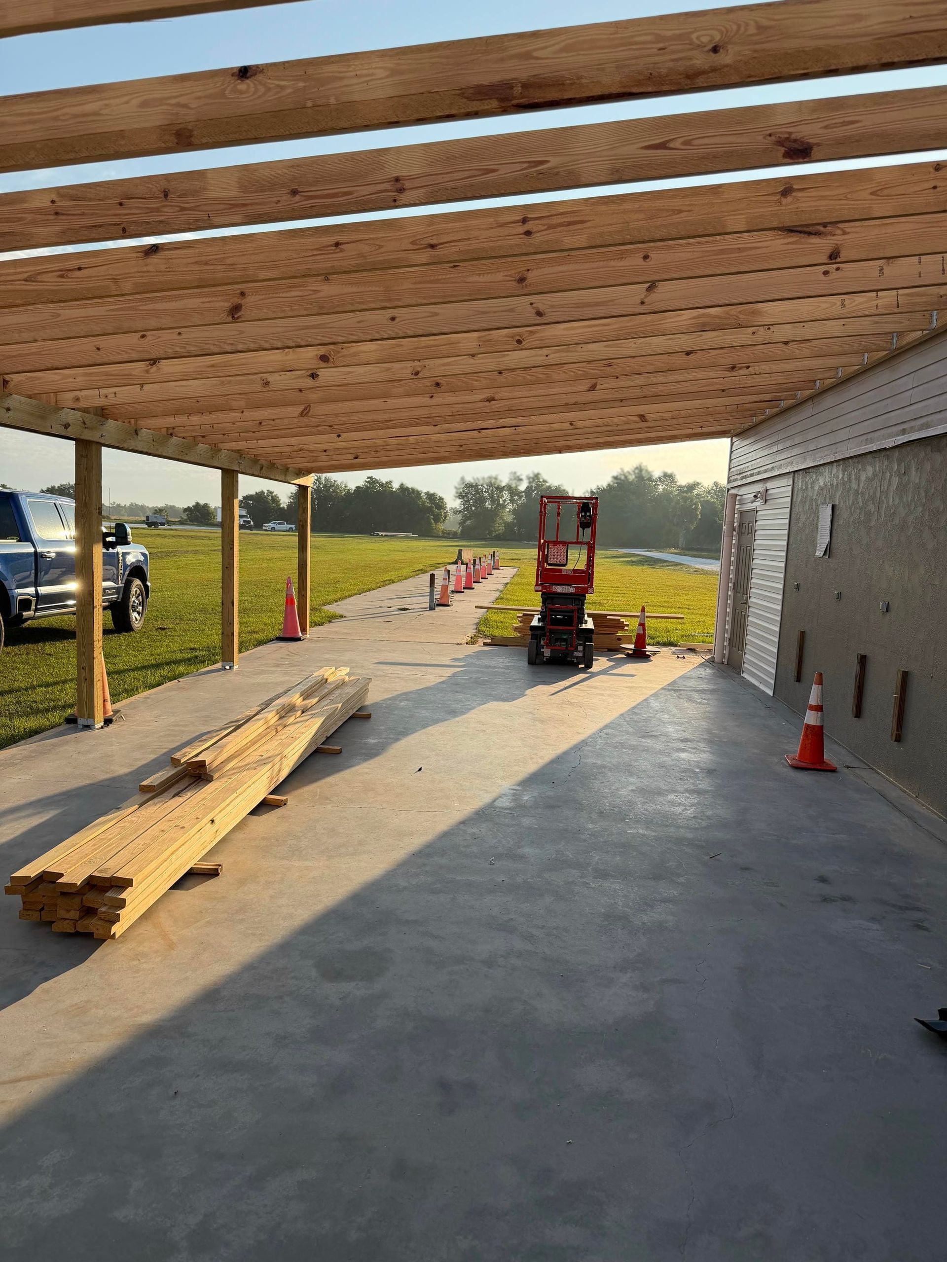 Partially built covered patio with wood ceiling, concrete floor, construction lift, and traffic cones