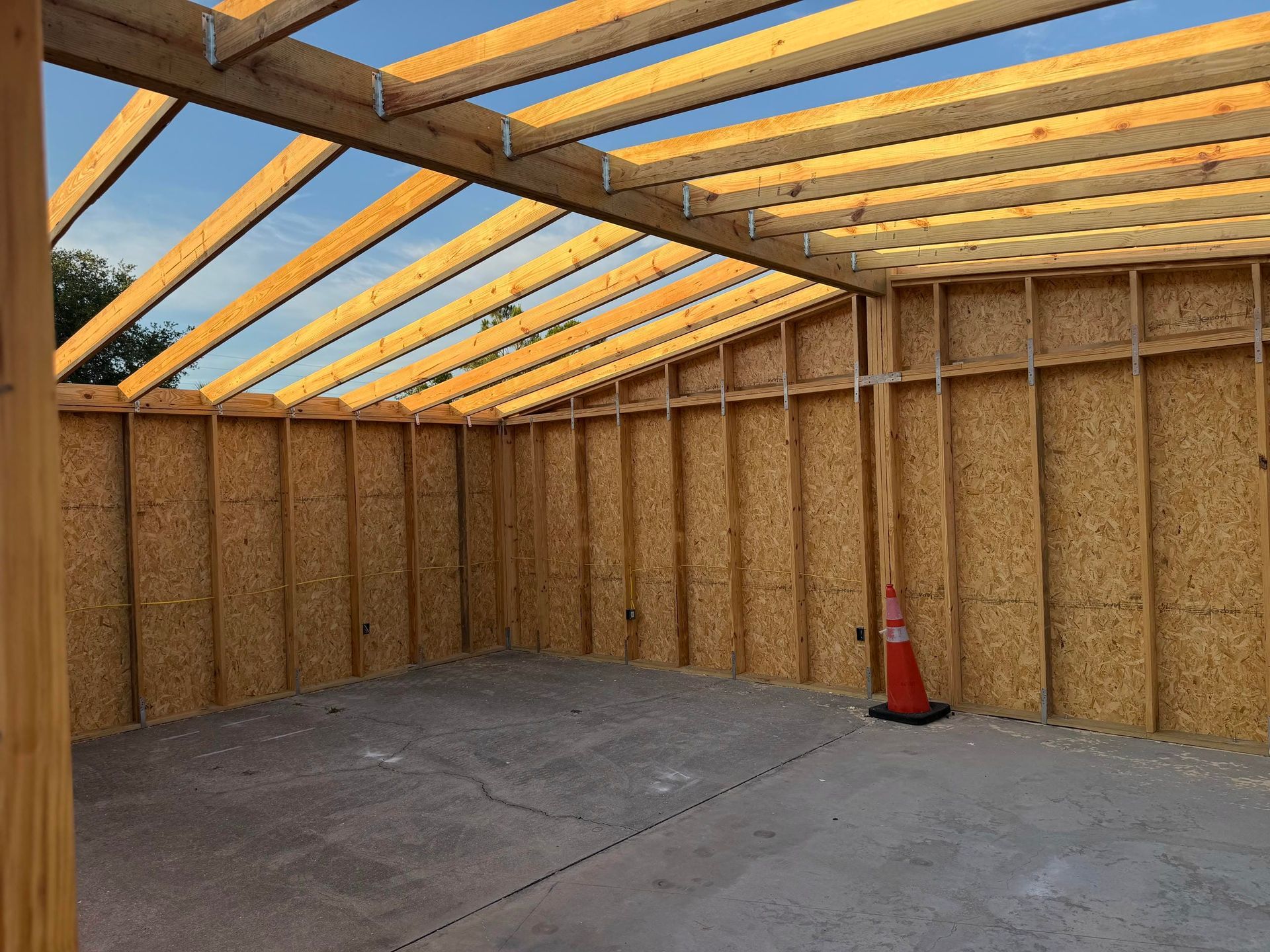 Interior of a partially built wooden shed with exposed framing, plywood roof panels, and a concrete floor