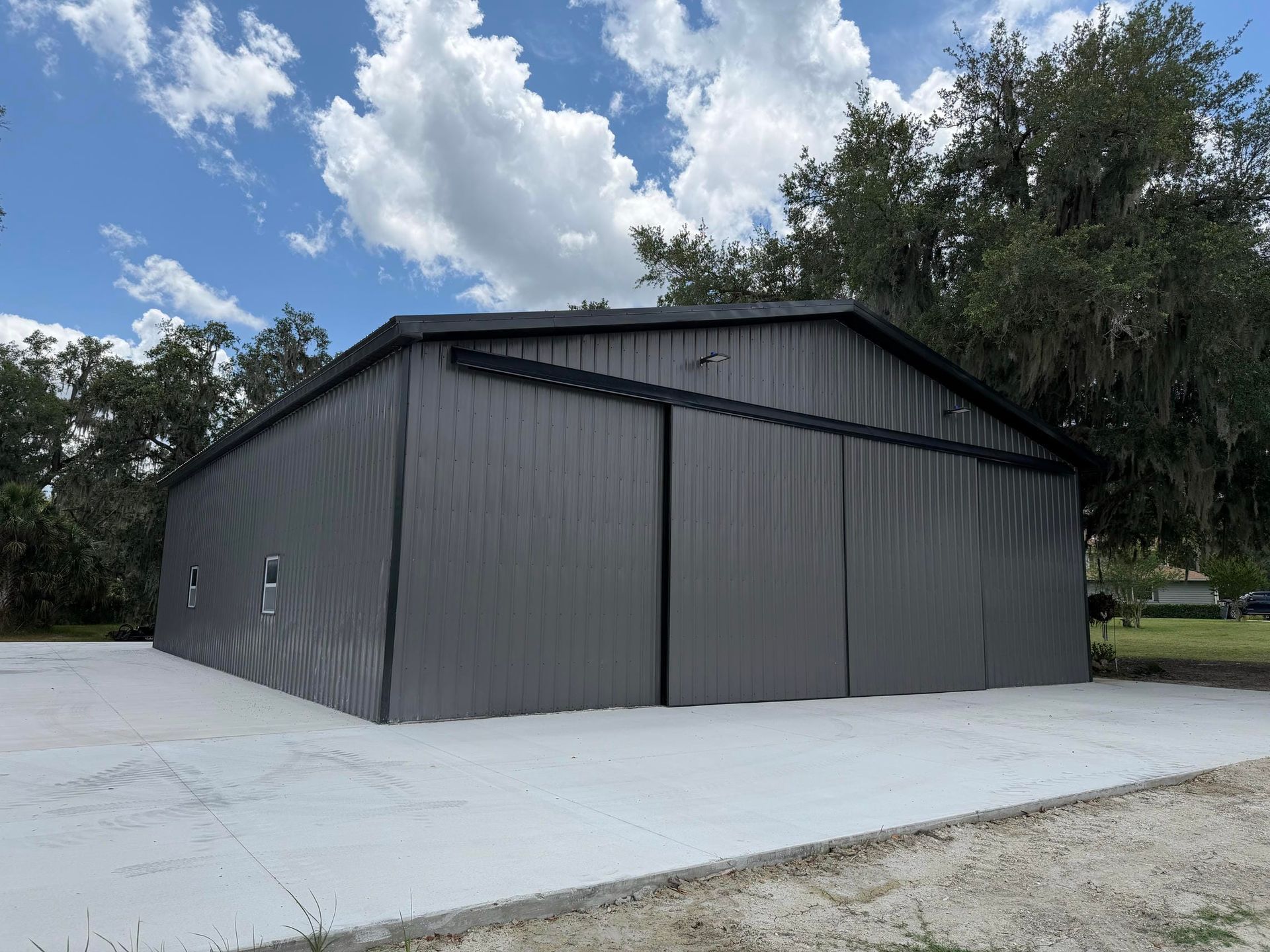 Gray metal warehouse with a peaked roof on a concrete lot under a partly cloudy sky