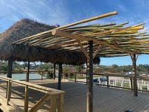 Thatched beachside deck with wooden railings and a palm-frond roof overlooking water and boats