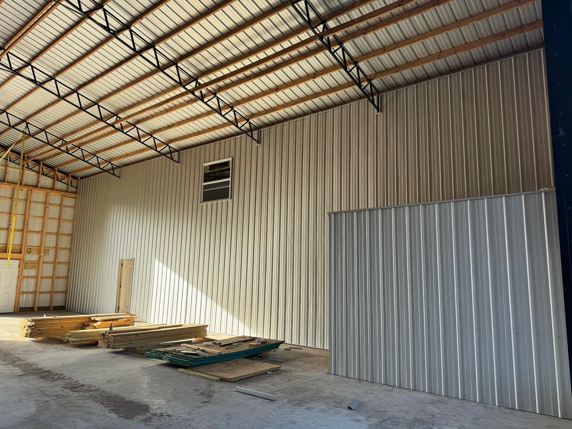Empty warehouse interior with corrugated metal walls, roof beams, and stacked materials on the floor