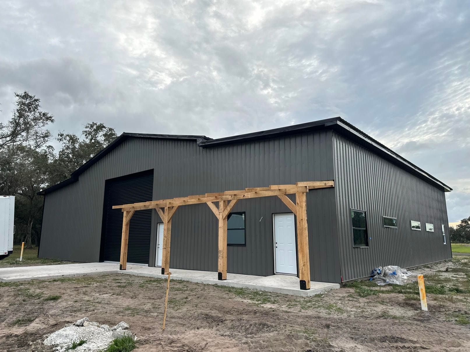 Dark gray metal building under construction with a wooden porch frame and cloudy sky