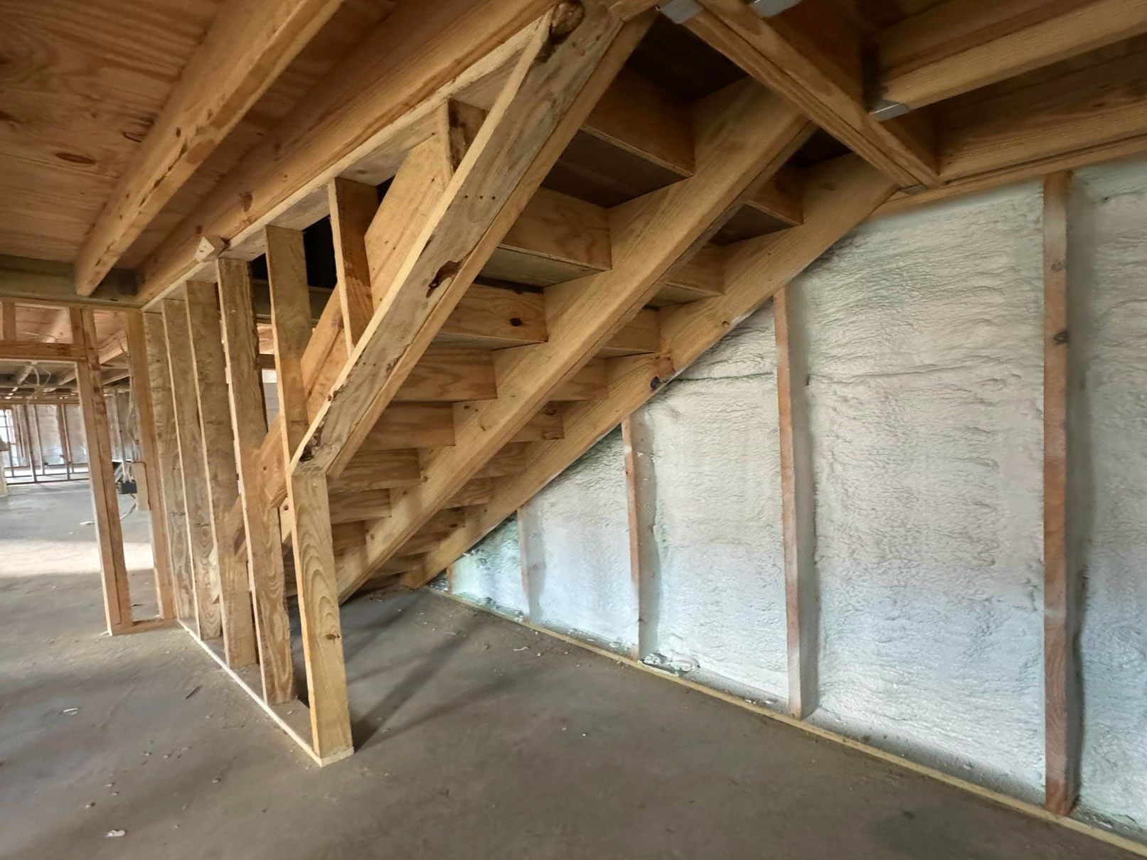 Wooden stair framing inside an unfinished house with exposed beams and white insulated wall panels.
