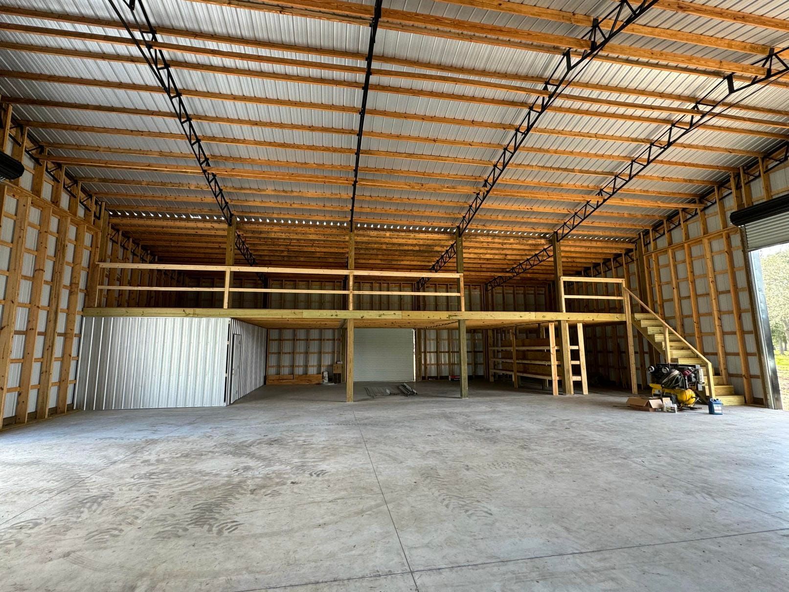 Empty warehouse interior with wooden mezzanine, exposed steel roof, and concrete floor