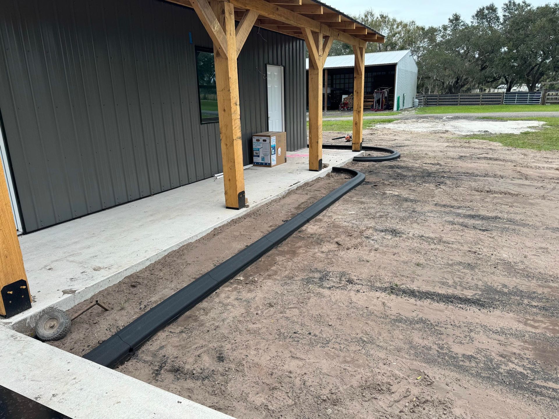 Covered building porch with wooden posts beside a dirt lot and curb along a concrete walkway.