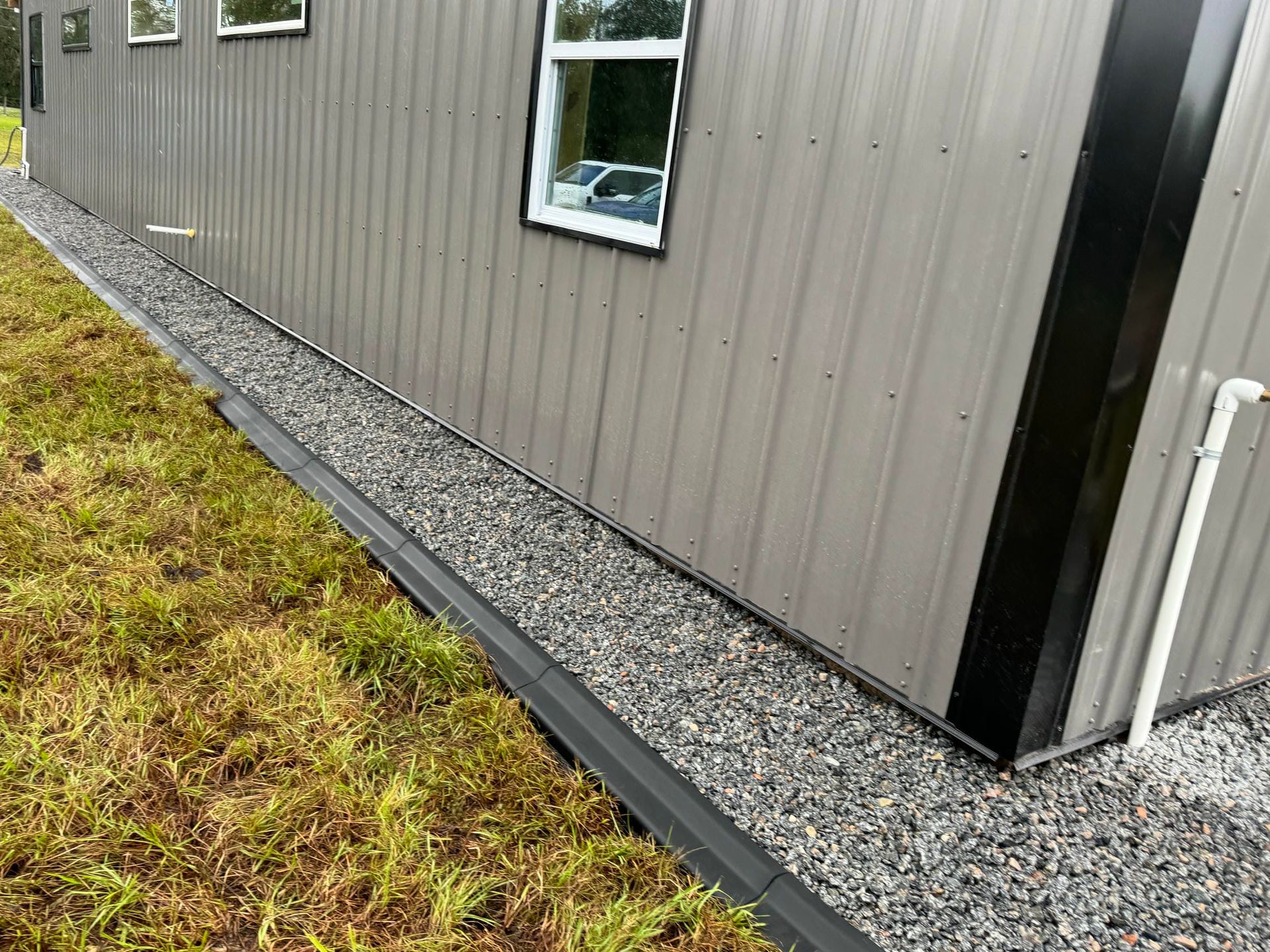 Gray metal-sided building with gravel border and small windows beside a grassy area
