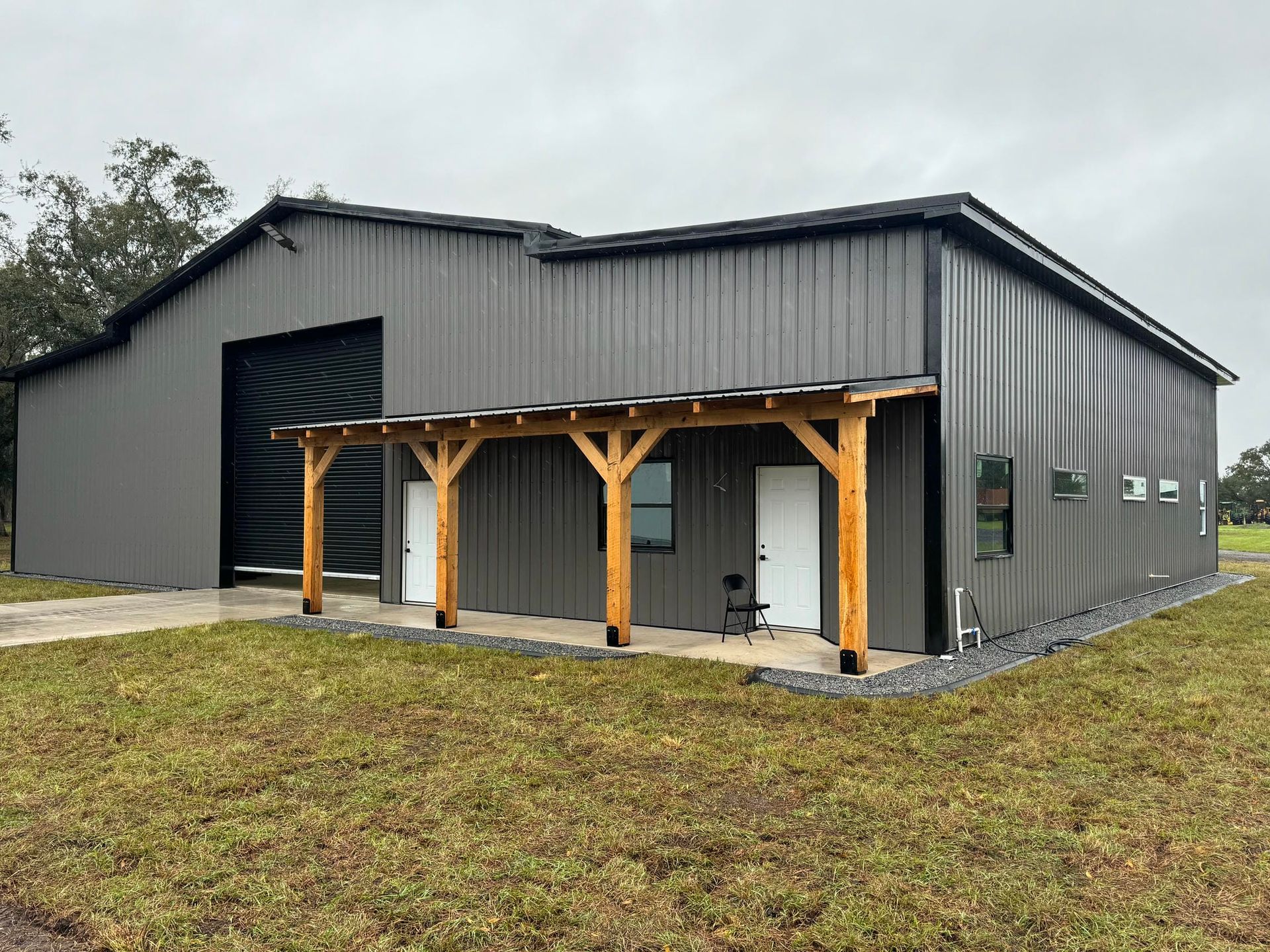 Gray metal barn with a covered porch and wooden posts on a grassy lot