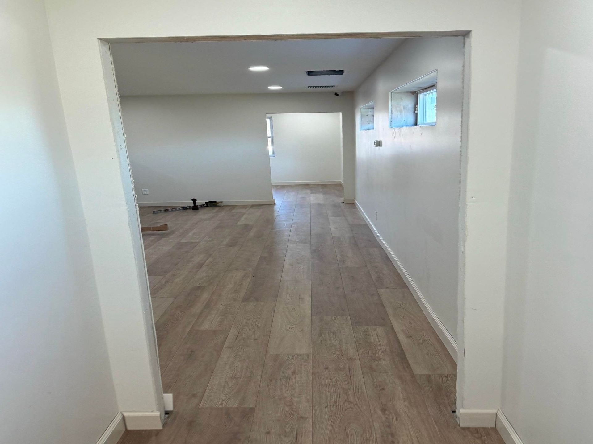 Empty modern hallway with wood flooring, white walls, and recessed ceiling lights, leading to a doorway.