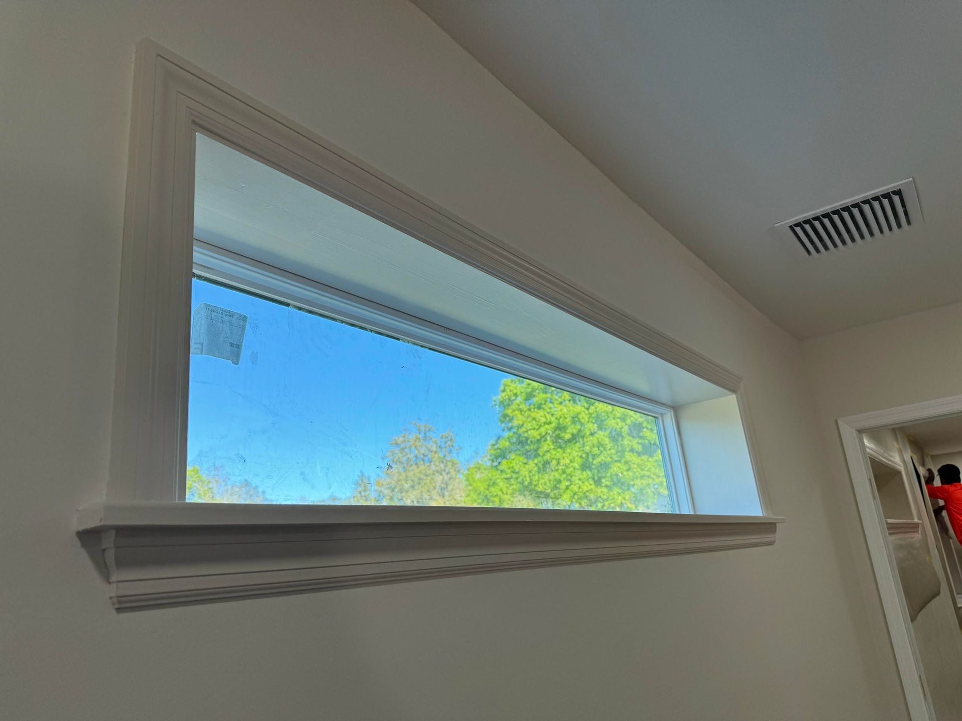 White-framed window in a light-colored room, showing blue sky and green trees outside.
