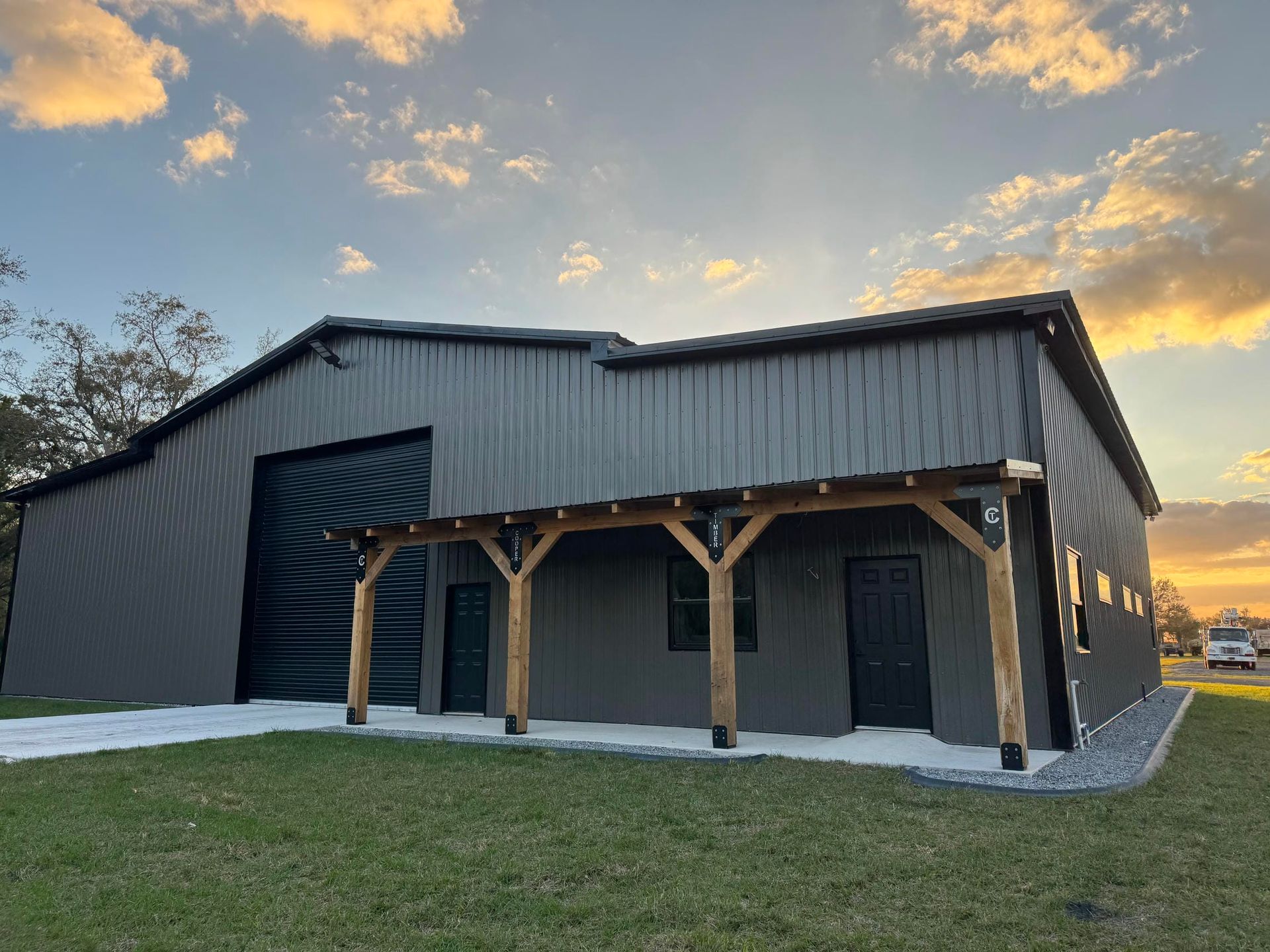Dark metal-sided barn with wooden porch posts at sunset on a grassy lot