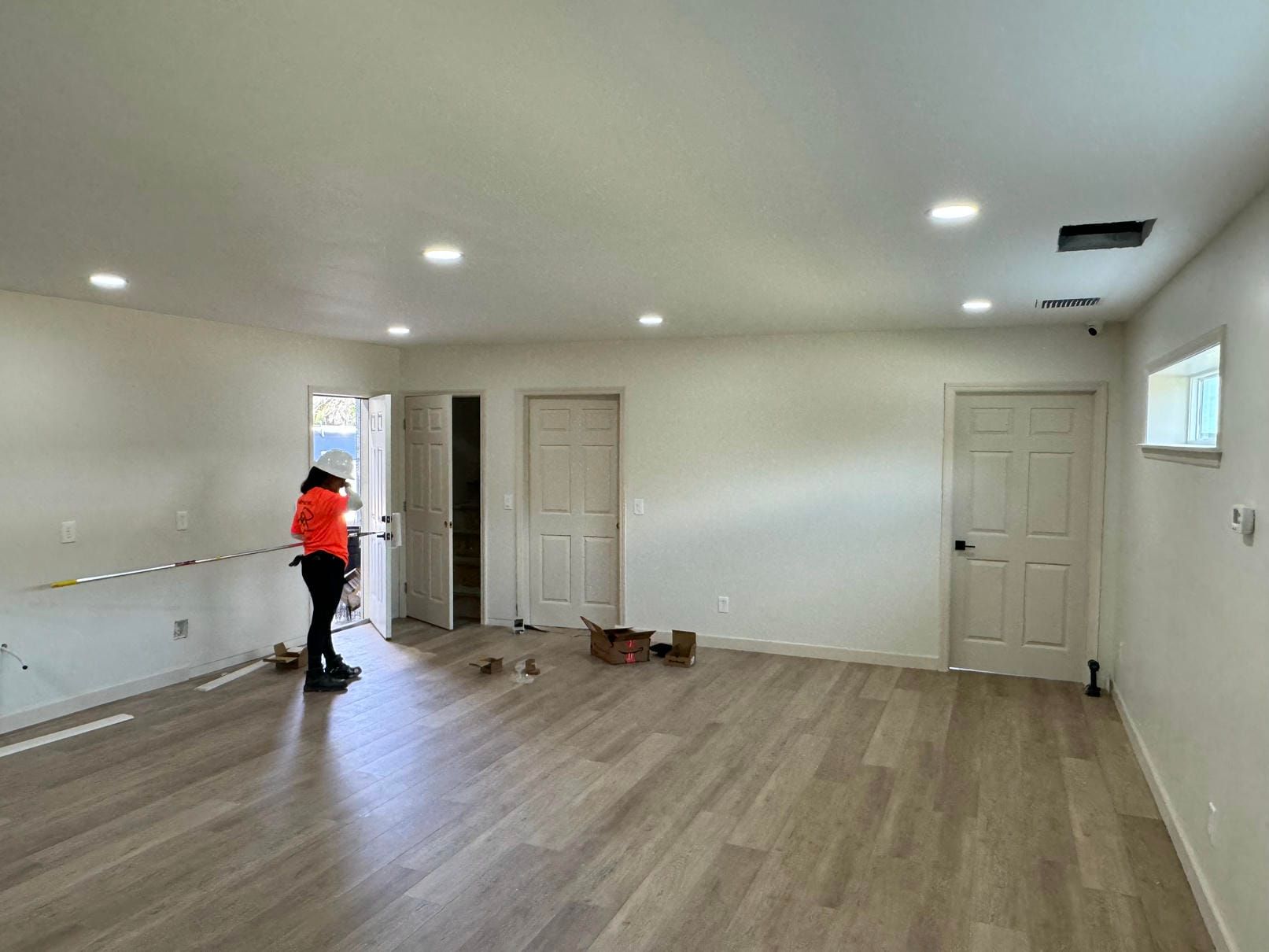 Person in orange shirt standing in empty room with wood floors and white walls during renovation