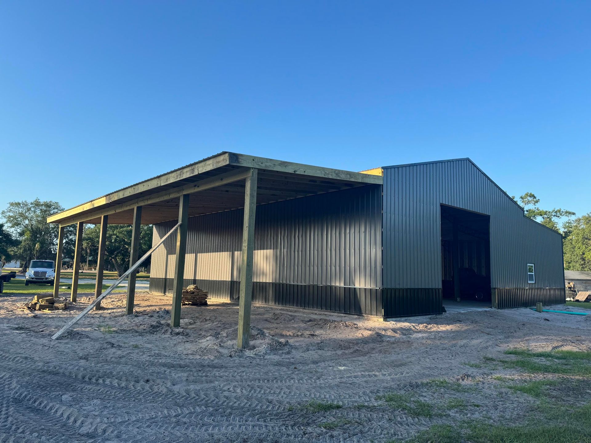 Large gray metal barn with a covered porch on a gravel lot under a blue sky