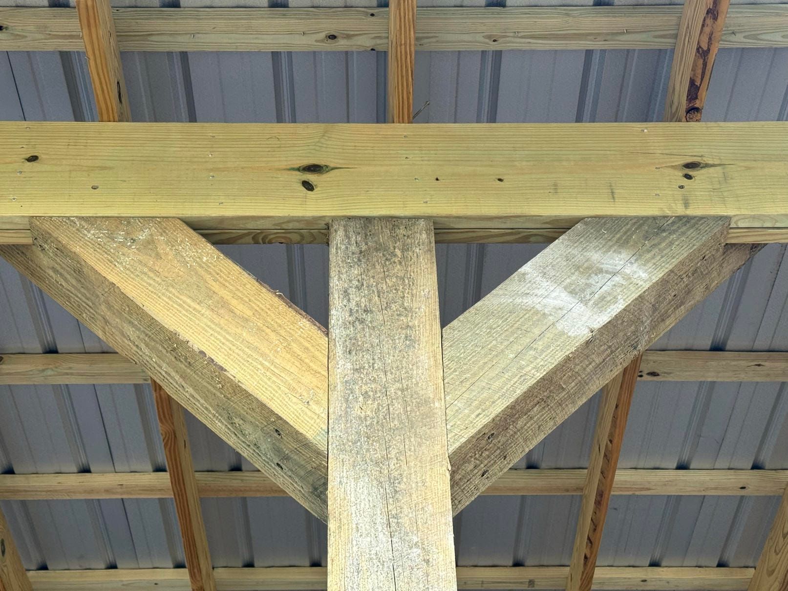 Wooden roof truss with diagonal braces under a corrugated metal ceiling