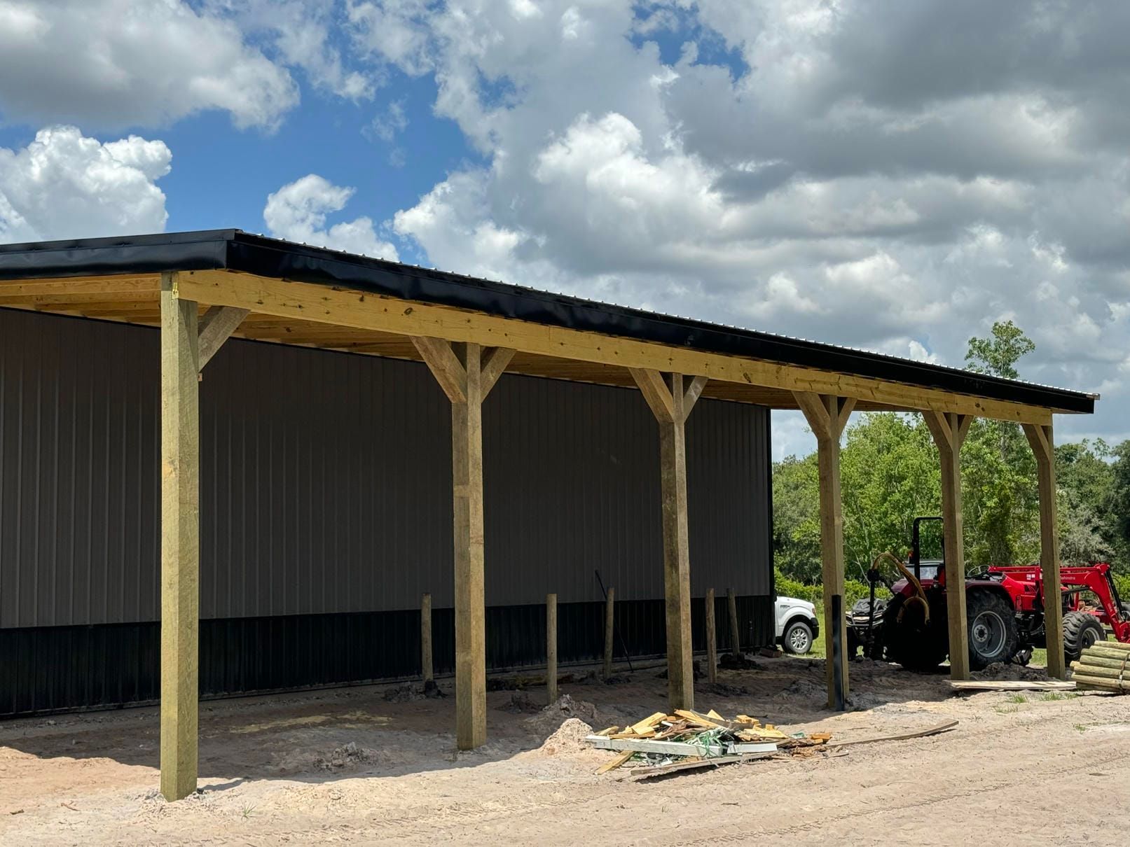 Wooden carport attached to a metal building, with a red ATV parked beside it under a cloudy sky.