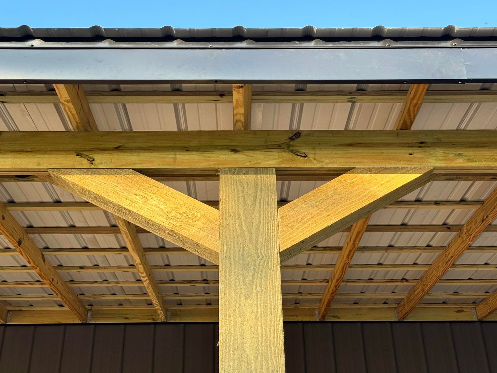 Wooden support post and braces under a roof, with yellow insulation and exposed beams.