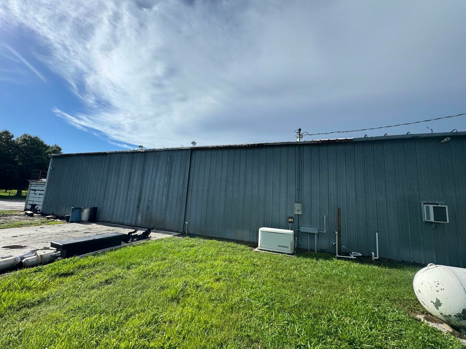 Gray industrial building with a grassy foreground and blue sky with wispy clouds