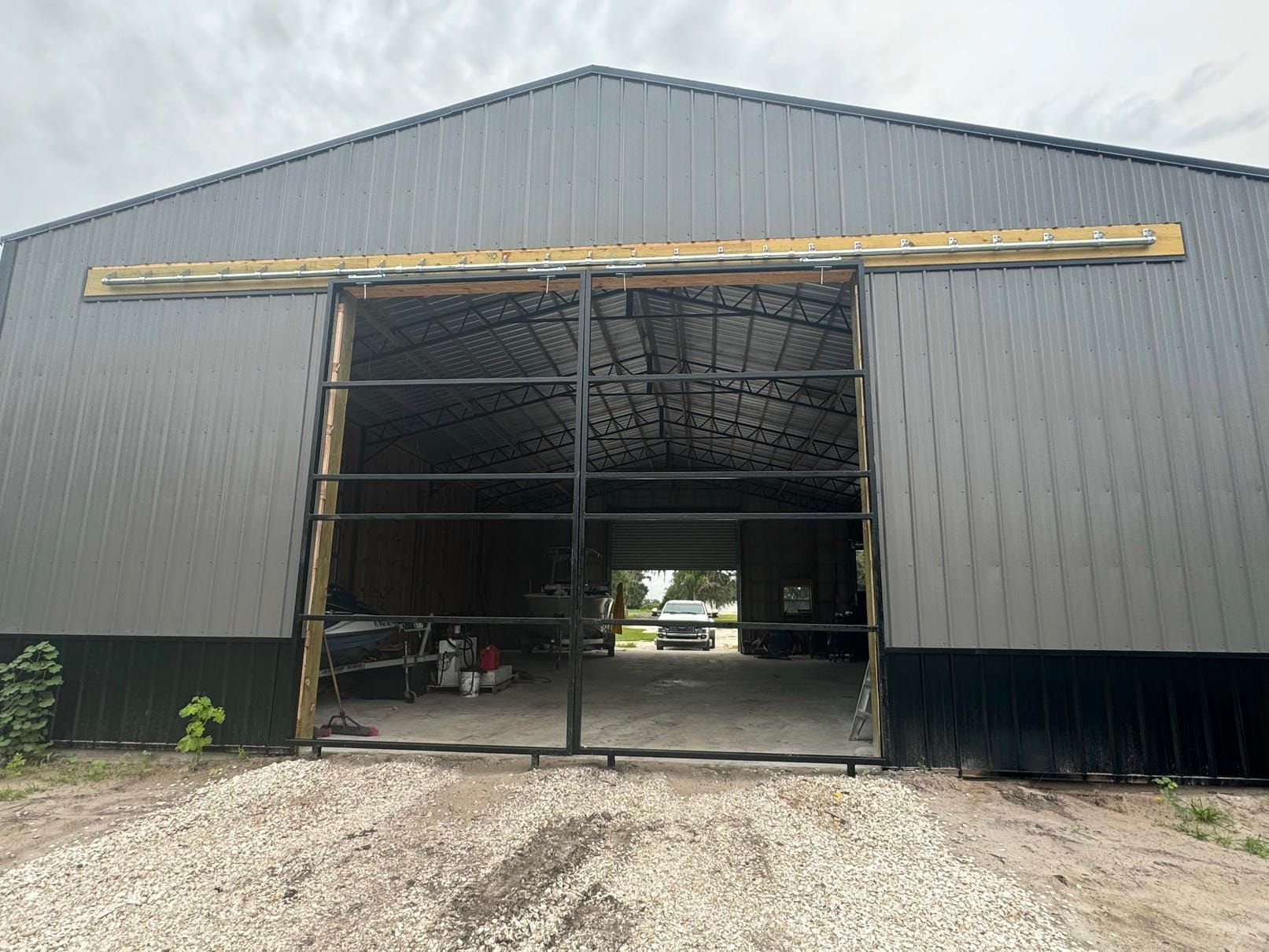 Large black metal barn with an open front, showing a partially visible interior and gravel driveway.