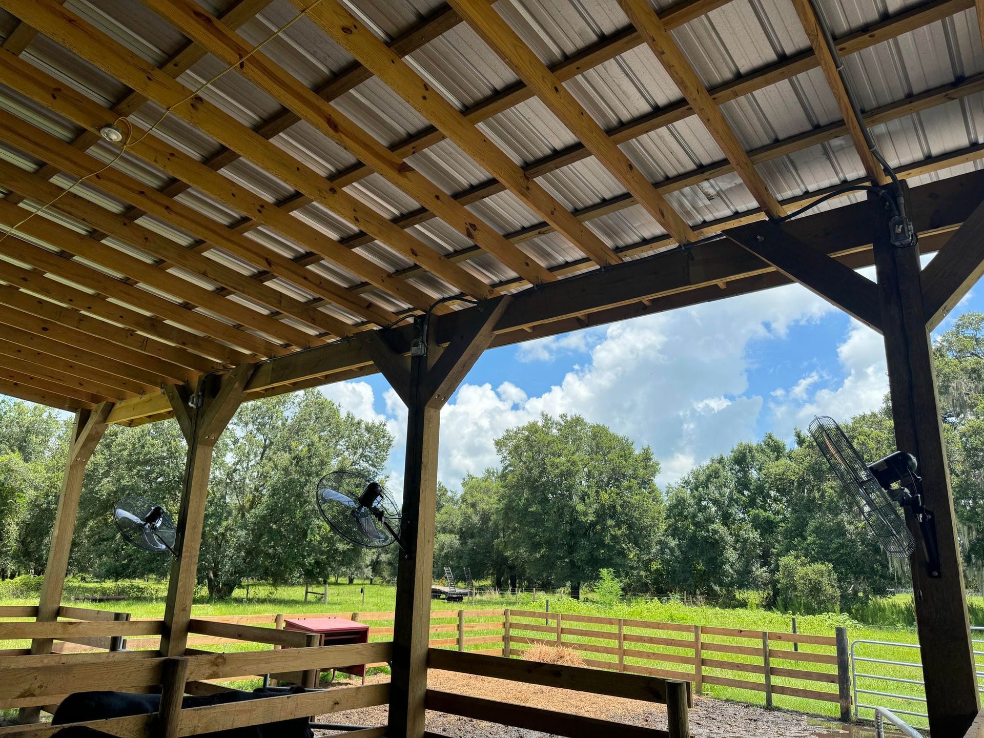 Covered wooden pavilion overlooking a green pasture and trees under a partly cloudy sky