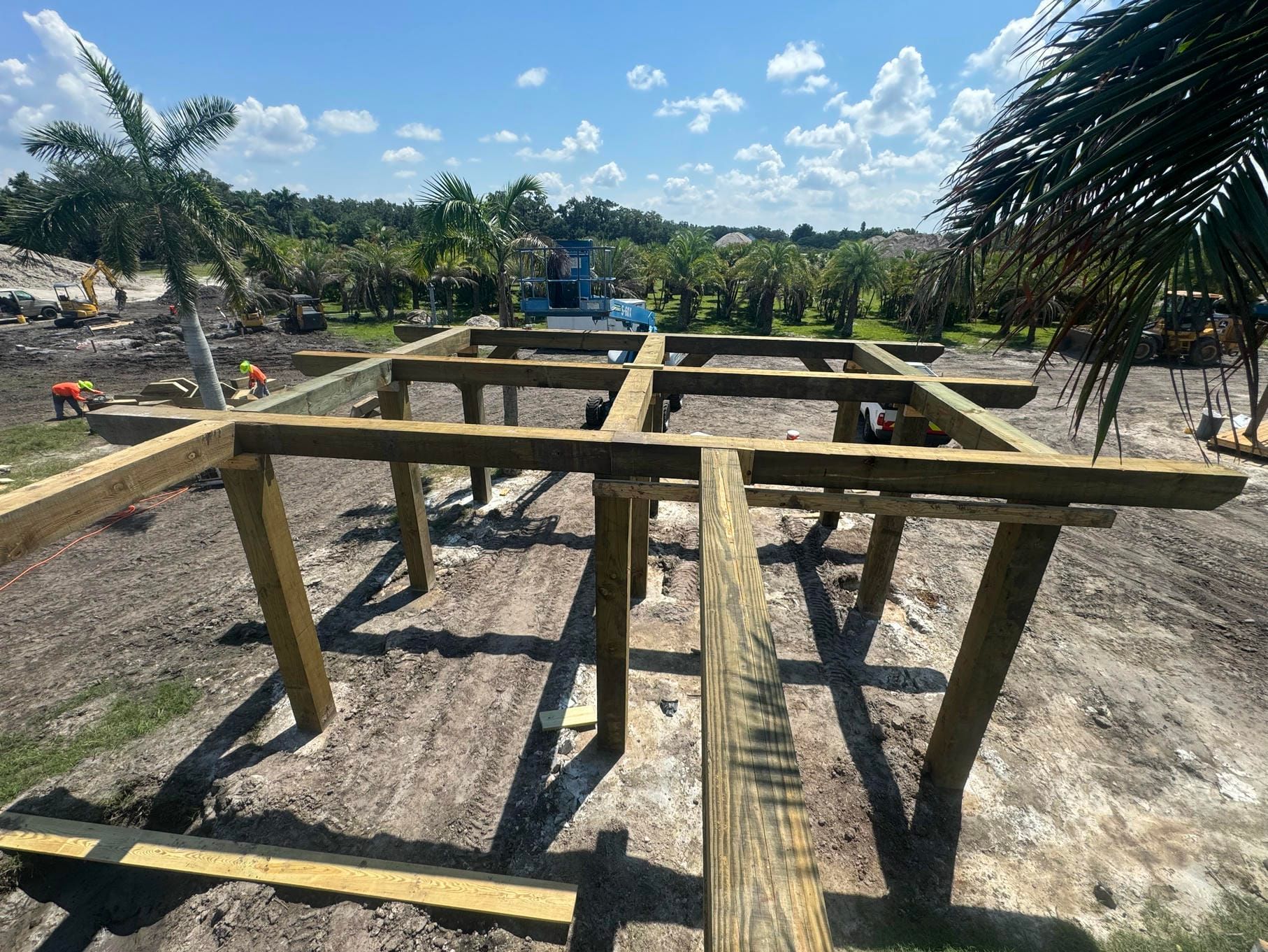 Wooden bench frames on a sandy outdoor site with palm trees and blue sky