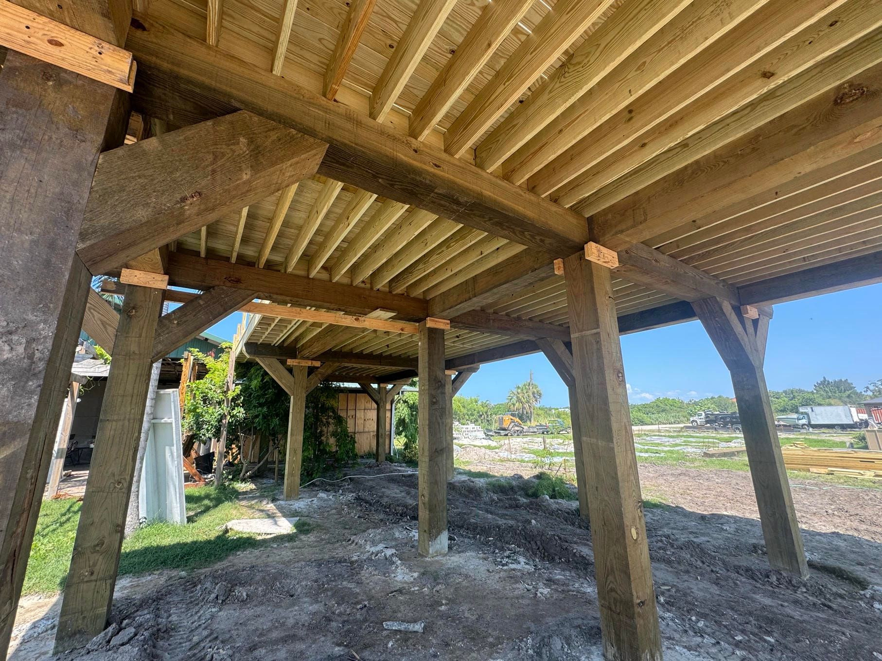 Wooden deck structure on stilts overlooking a grassy waterfront area under clear blue sky