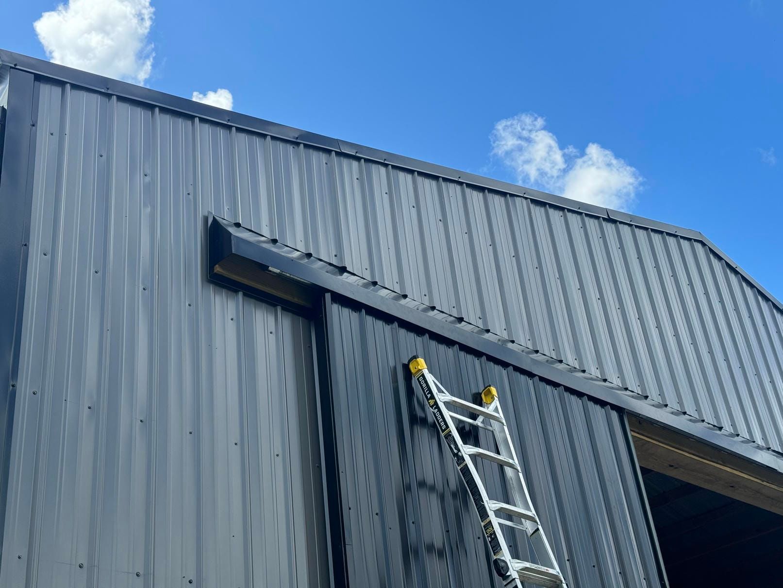 Metal-clad building with a ladder leaning against the roof edge under a blue sky