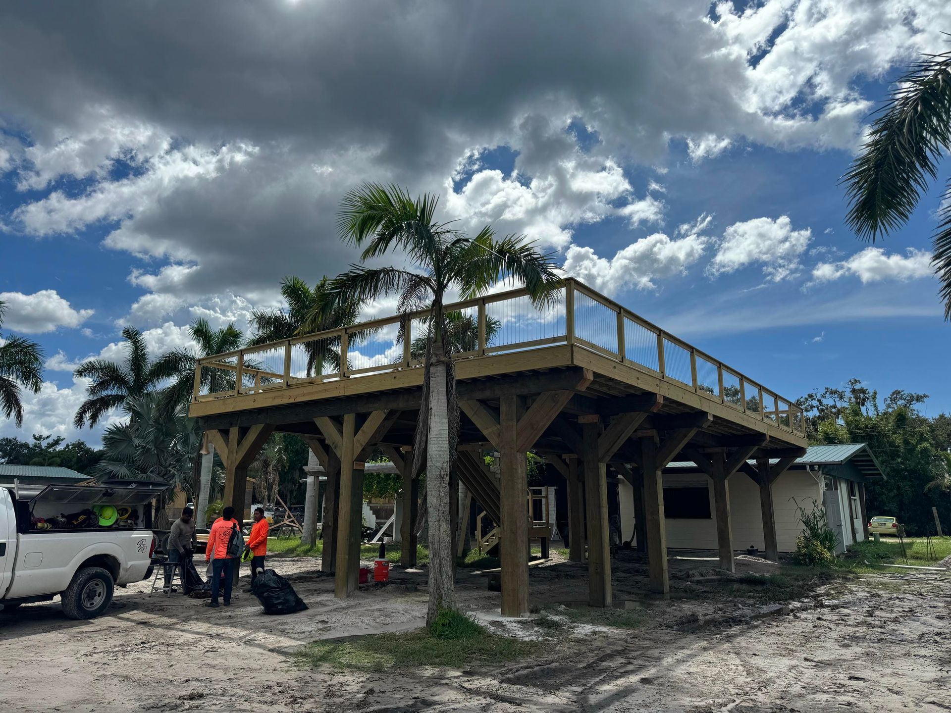 Partially built wooden house on stilts with workers and a truck under a cloudy sky