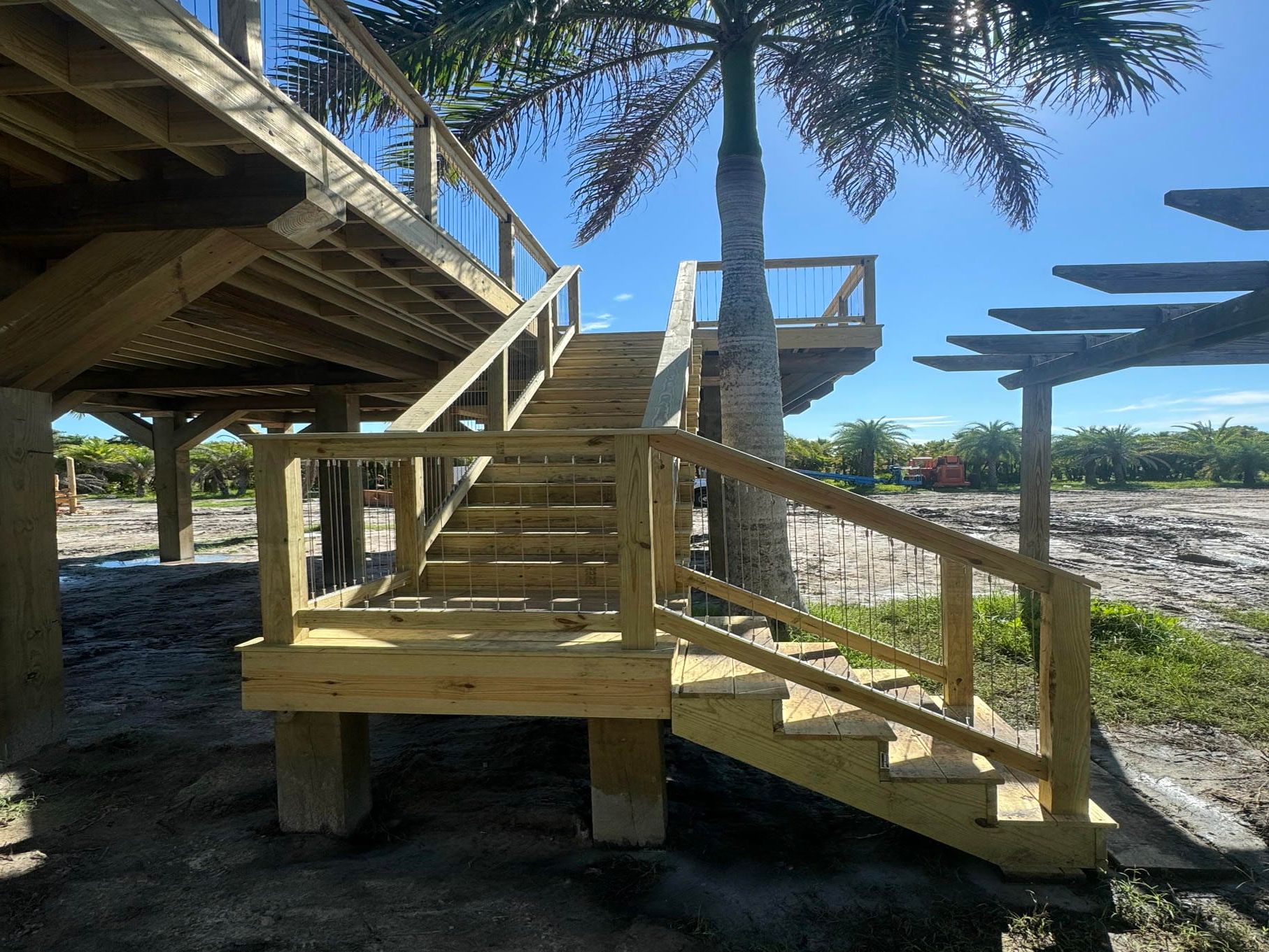 Wooden beach stairs and ramps under palm trees in bright sunlight