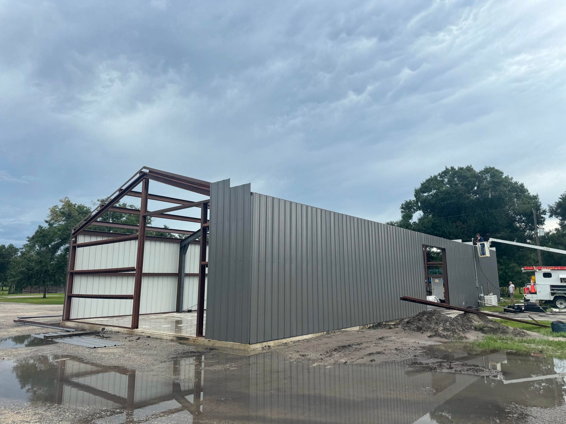 Partially built metal shed beside muddy puddles under a cloudy sky