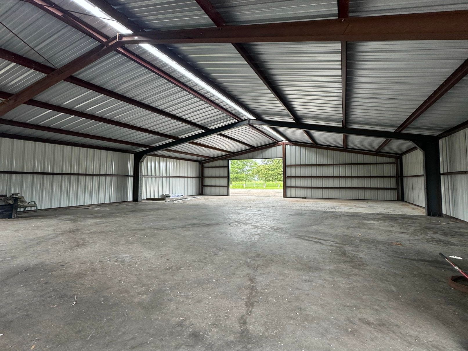 Empty metal-roofed warehouse interior with concrete floor and open doorway to outside