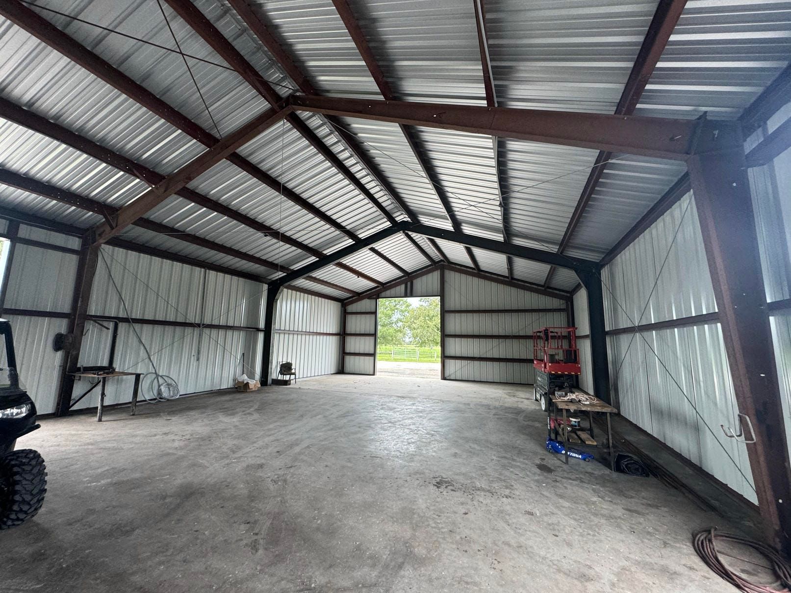 Spacious metal barn interior with gravel floor, open front, and tools along the walls