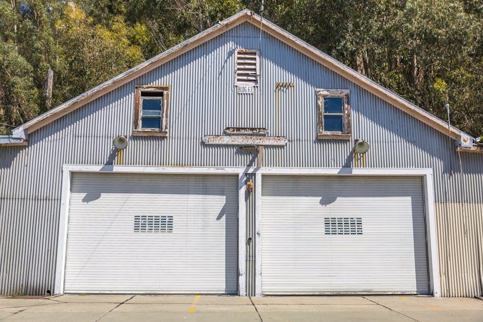 Two white garage doors on a gray barn-style building with blue trim and a peaked roof.