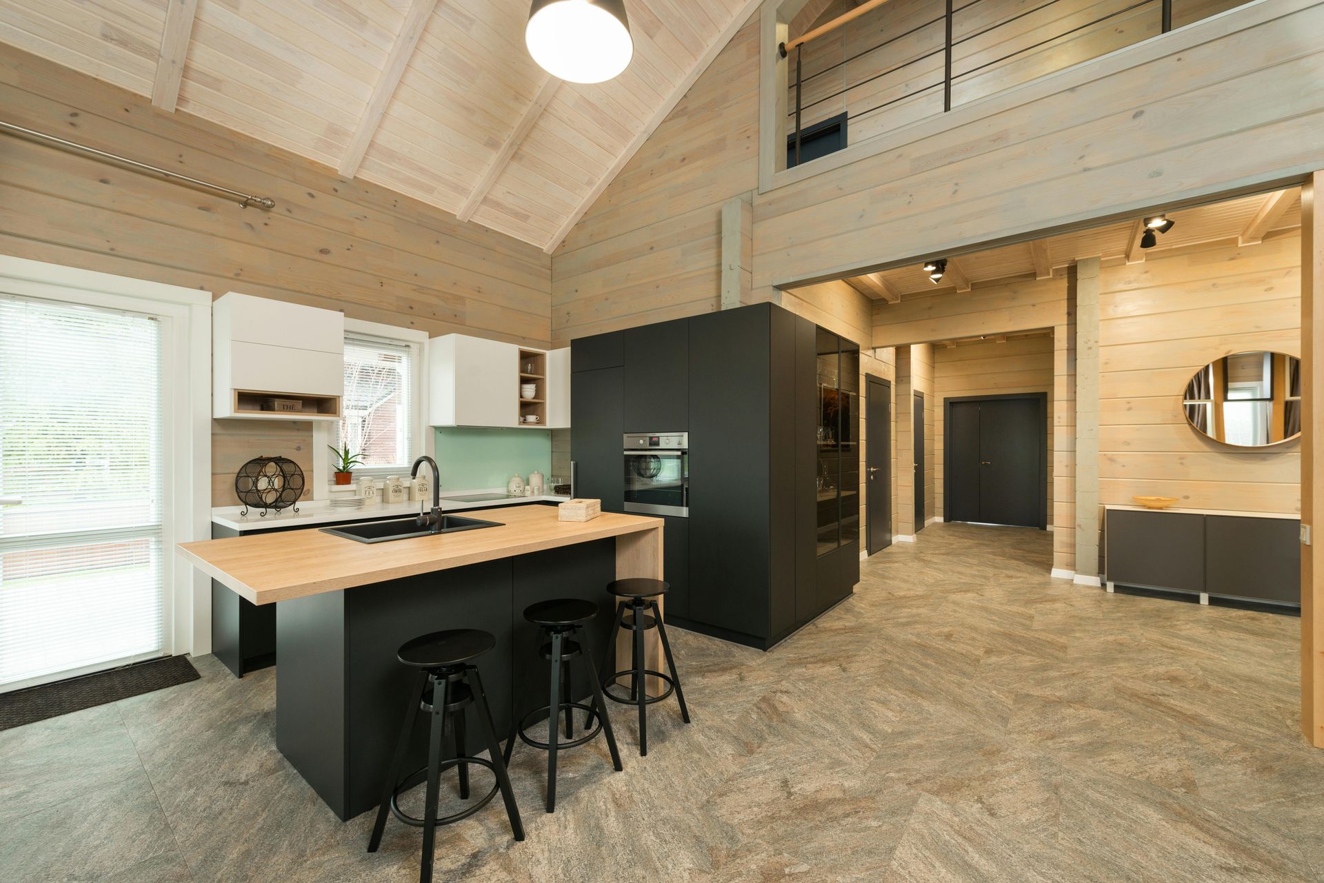 Modern loft kitchen with black island, stools, wood beams, and a mezzanine walkway