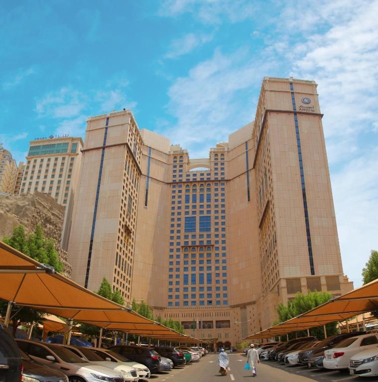 Large beige building with cars parked underneath beige canopies, against a blue sky.
