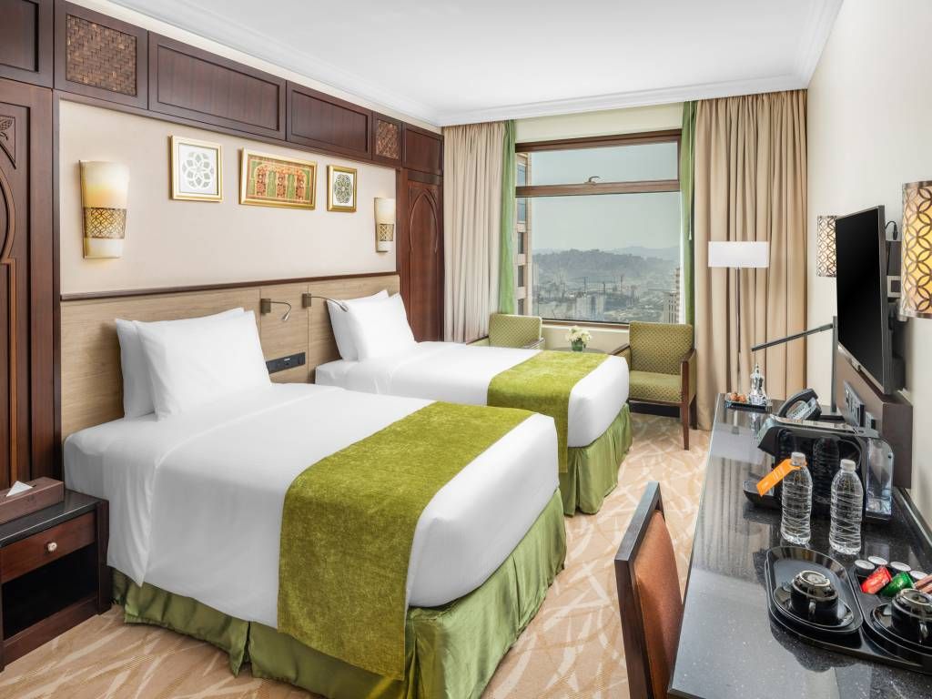 Hotel room with two twin beds, desk, and a window with a city view.