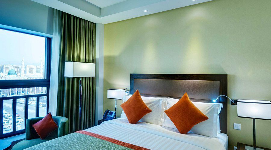 Hotel bedroom with bed, pillows, window, and green and orange accents.