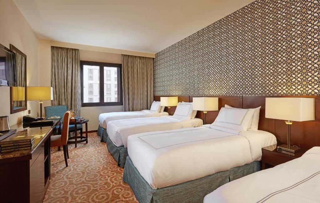 Hotel room with four twin beds, patterned accent wall, desk, and window.