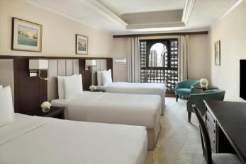 Hotel room with three single beds, a window, a chair, and a desk.