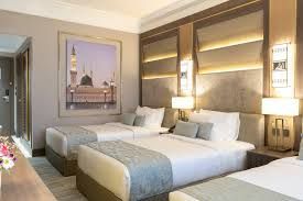 Hotel room with three beds, a picture of a mosque, and bedside lamps.